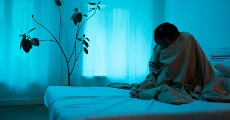 Sad woman seating on bed in risks of eating disorders.